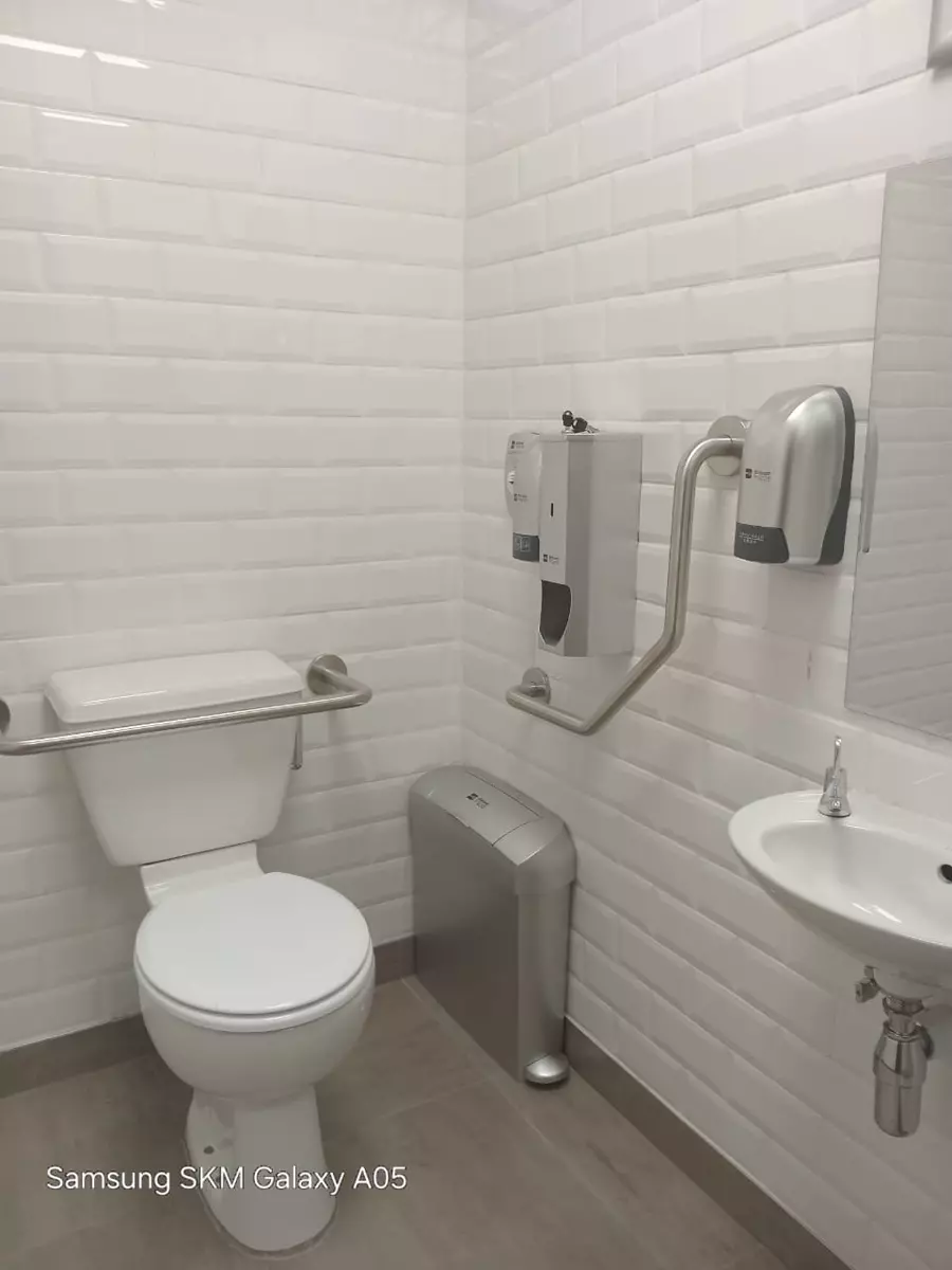 Clean accessible public restroom with white toilet, grab bars and sink — example of plumbing installation work
