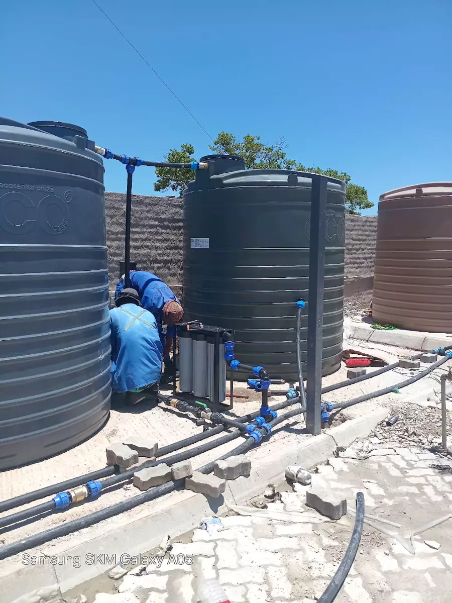 Workers installing large industrial water tanks and a filtration system outdoors