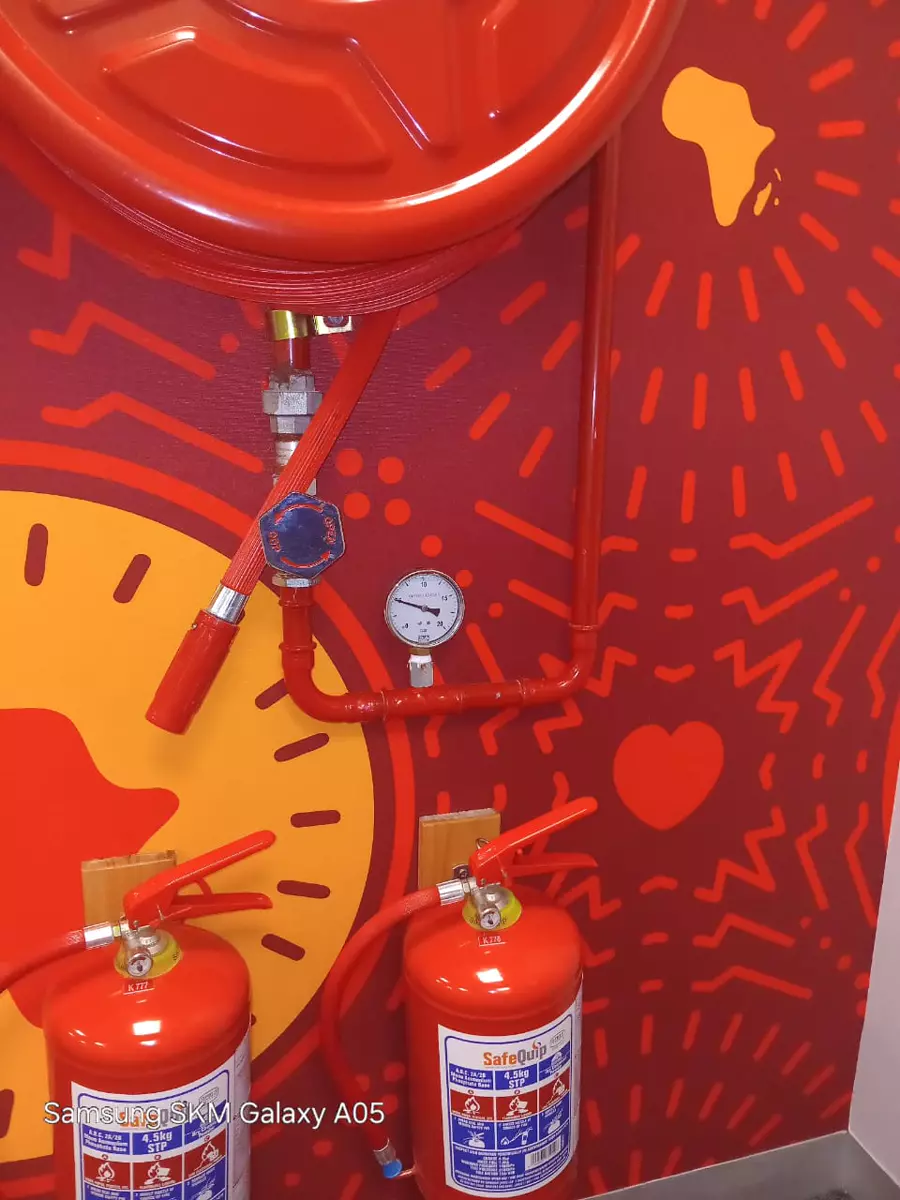 Fire safety equipment including a fire hose reel, pipes and fire extinguishers mounted on a red and yellow wall